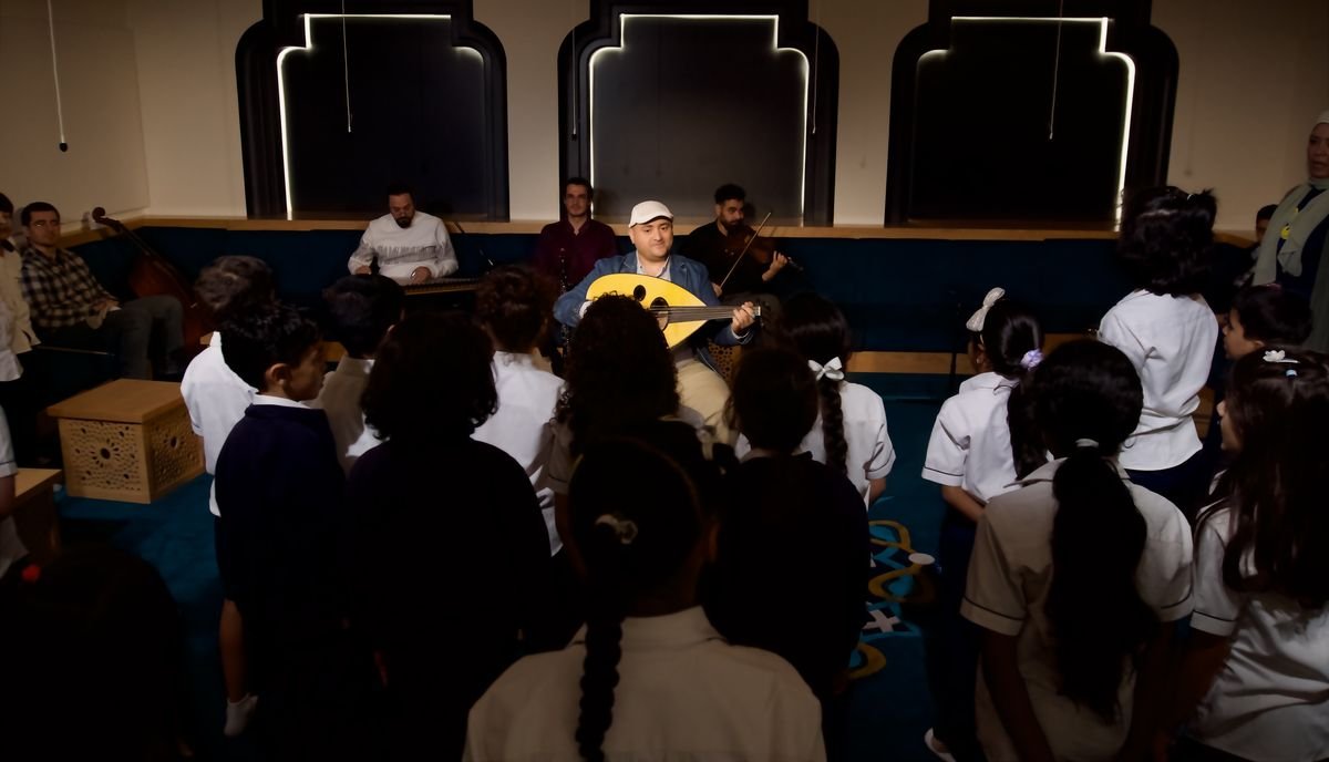 Wael Salah playing oud for students at a music workshop, with musicians behind him